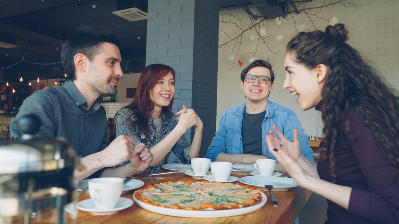 Services Group of four friends laughing and enjoying pizza and coffee together in a cozy cafe.