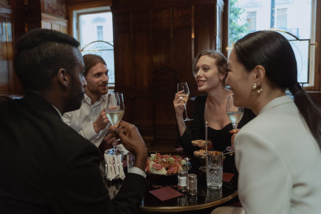Services A diverse group of friends enjoying drinks and dinner in a stylish restaurant setting.