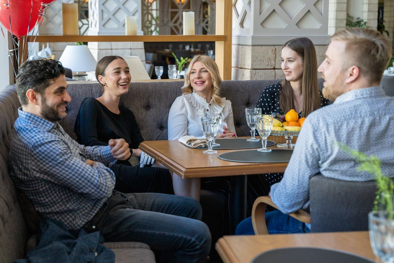 Services Five adults having a joyful conversation in a cozy restaurant setting indoors.
